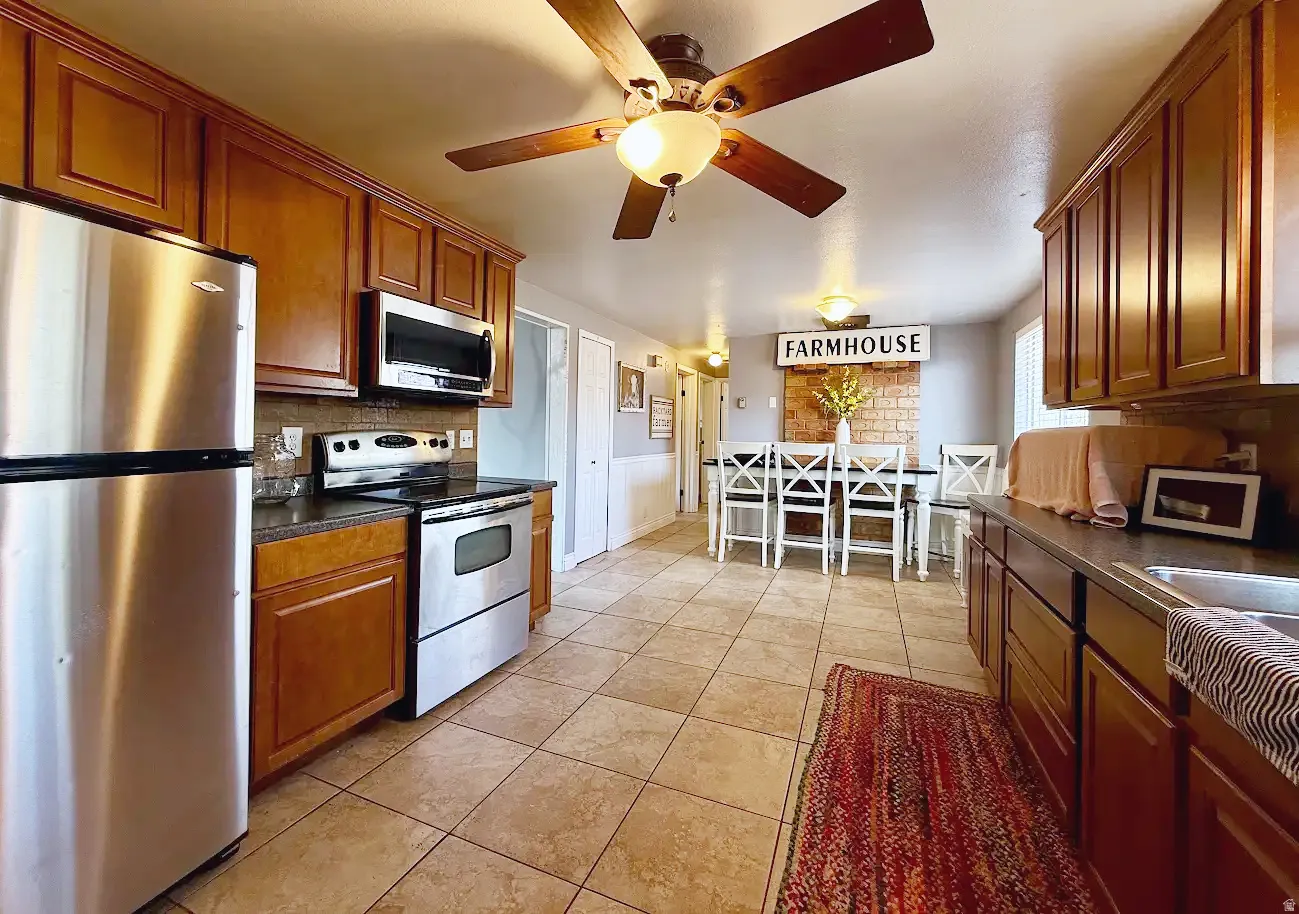 Wood-finish cabinetry, stainless steel appliances, tile flooring, and a ceiling fan with integrated lighting