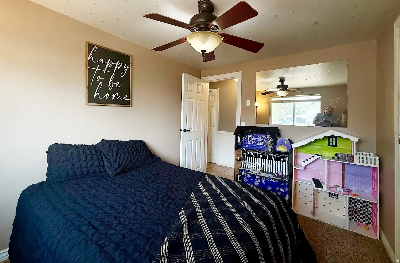 Wall-mounted mirror reflecting natural light, ceiling fan with integrated lighting, and a white interior door with black hardware