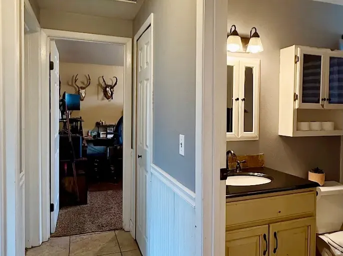 Tile flooring, beadboard wainscoting, built-in vanity with dark countertop, vanity mirror, wall-mounted lighting