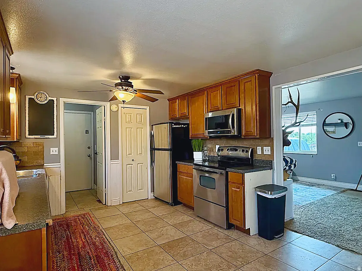 Kitchen featuring tiled flooring, wood cabinetry, stainless steel appliances, and a ceiling fan