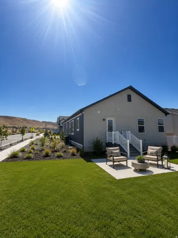 Expansive green lawn with a concrete patio, white railing, and exterior lighting
