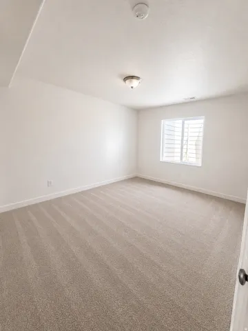 Bright secondary bedroom featuring neutral carpet flooring, white painted walls, and abundant natural light from a shuttered window