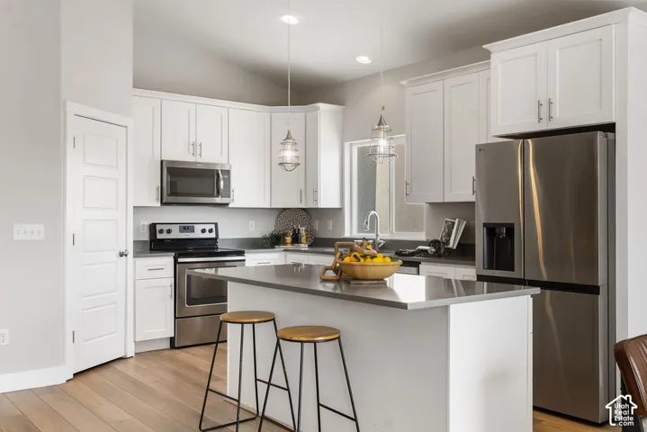 Modern kitchen featuring white shaker cabinetry, stainless steel appliances including a side-by-side refrigerator and built-in microwave, quartz countertops, a waterfall-edge island with seating for two, pendant lighting, pantry and wood-finish flooring