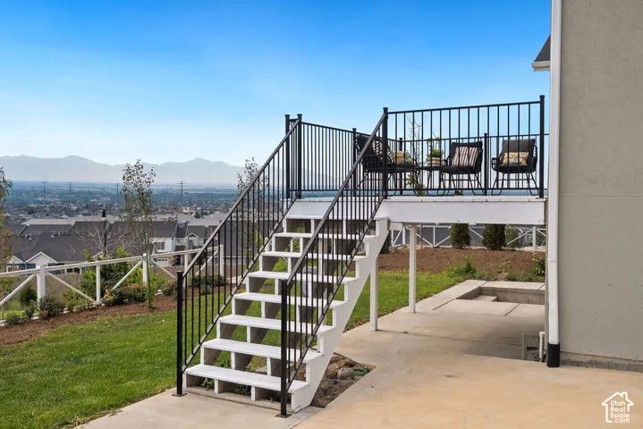 Upper-level deck with black metal railing, white stairs, and a concrete patio below