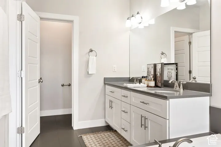 Spa-inspired primary bathroom featuring a dual-sink vanity with white cabinetry, gray quartz countertops, and polished chrome hardware