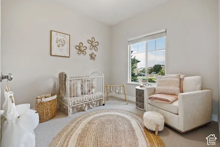 Bright nursery featuring abundant natural light from large picture windows, neutral wall finishes, hardwood flooring, and a circular woven area rug
