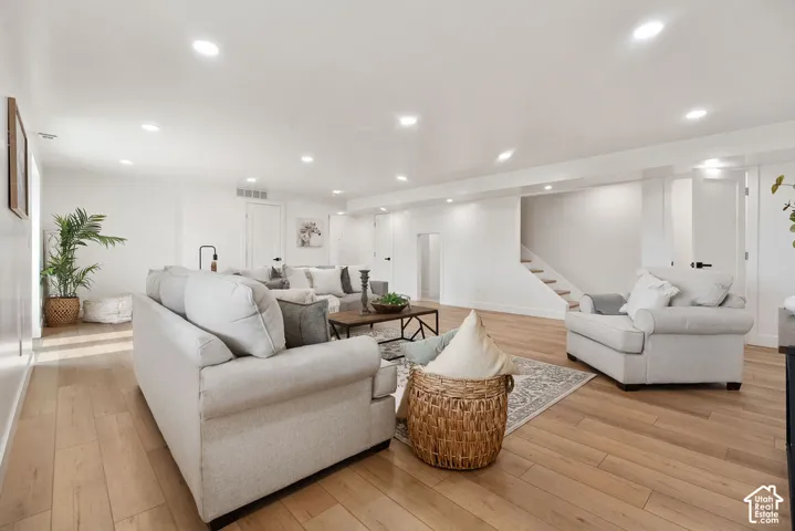 Spacious open-concept living area featuring pristine wood-finish flooring throughout, recessed ceiling lighting, and multiple seating zones anchored by upholstered sofas