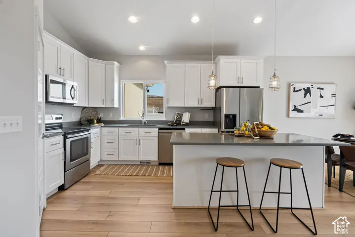 Modern kitchen featuring white cabinetry, stainless steel appliances, and a gray quartz island countertop with seating for two
