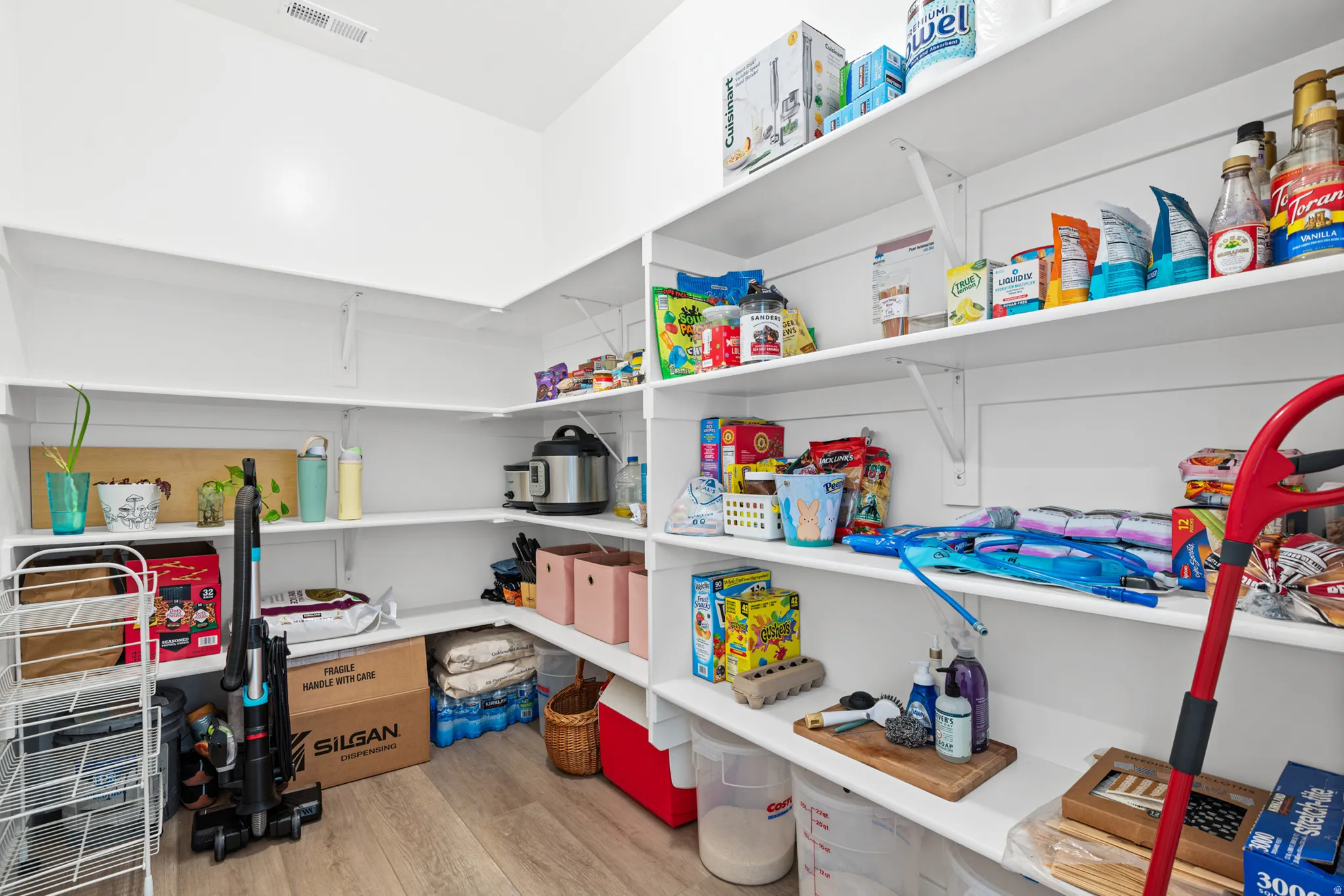 Organized pantry featuring extensive built-in shelving with multiple tiers, wood-finish flooring, recessed ceiling lighting, and ample storage capacity for pantry essentials and household supplies