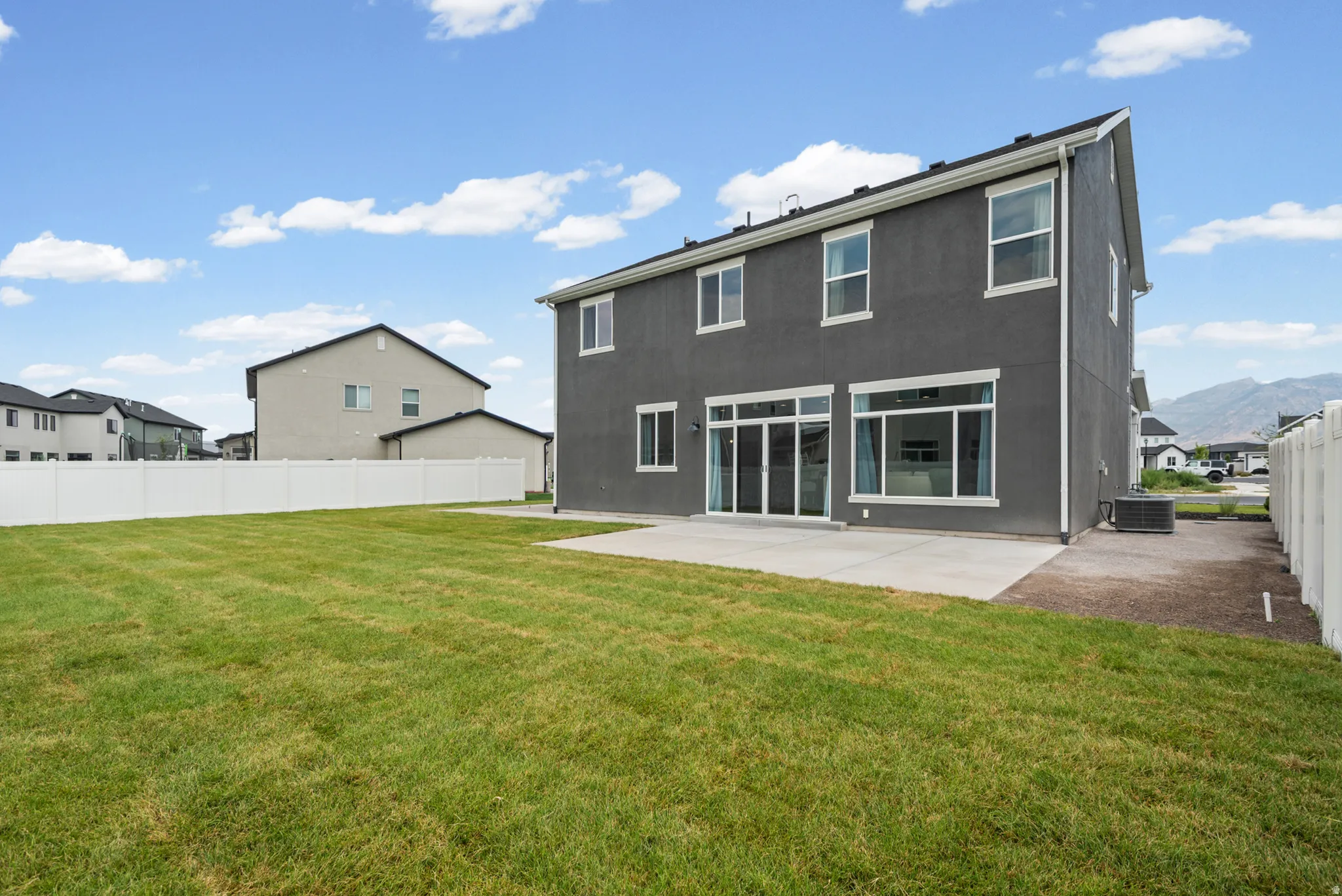 Expansive green lawn, concrete patio, white privacy fence, and multi-story home with large windows