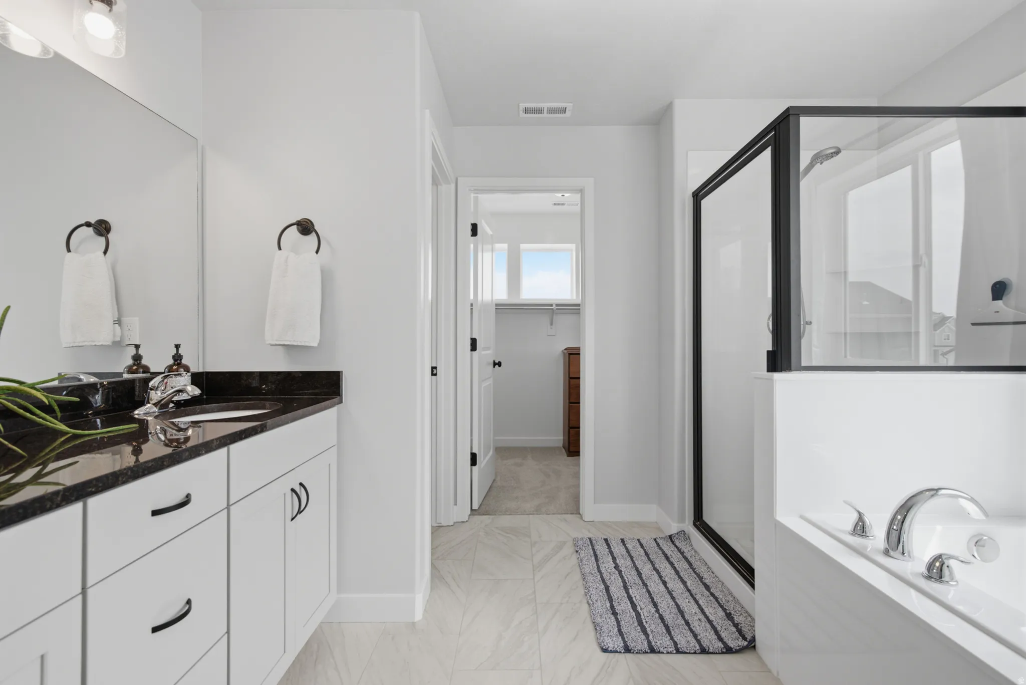 Dual vanity with dark stone countertop, white cabinetry with dark hardware, walk-in shower with black-framed glass enclosure, and a built-in soaking tub
