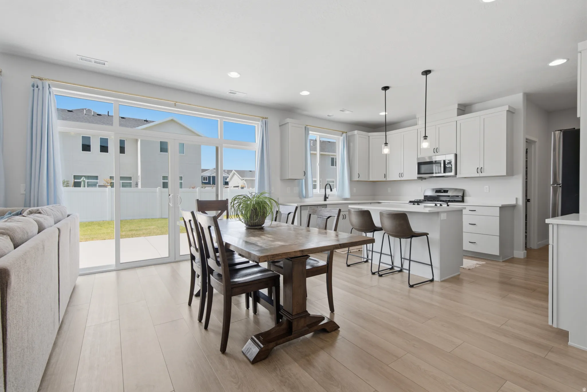 Open-concept living and dining area featuring wood-finish flooring, a pedestal dining table with seating for six, and expansive glass sliding doors opening to an outdoor patio