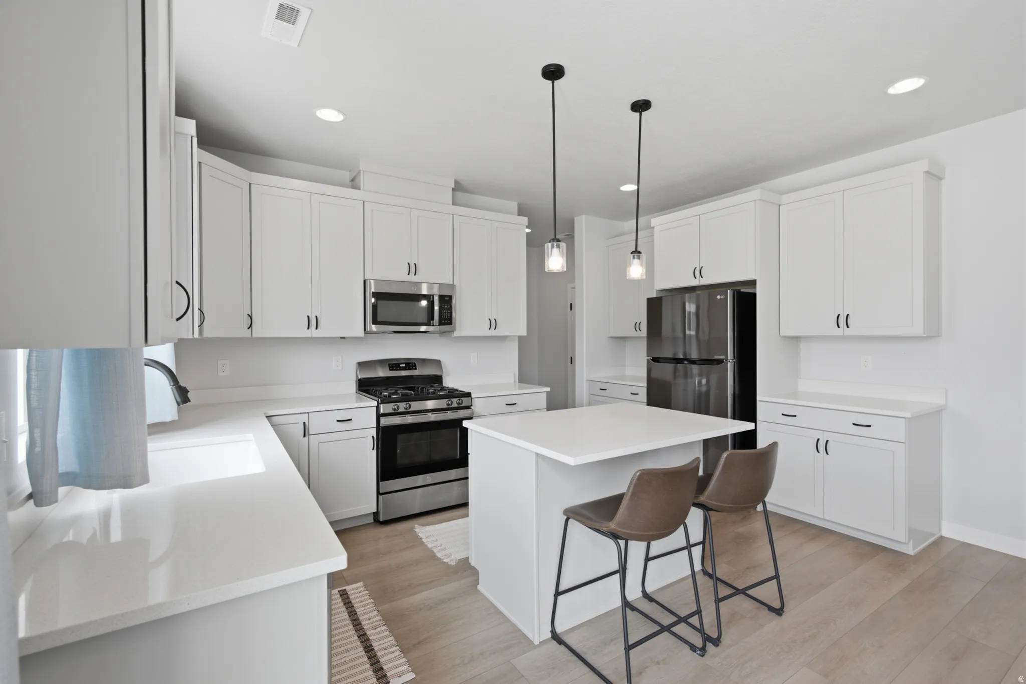 Bright kitchen featuring white cabinetry, light countertops, stainless steel appliances, and wood-finish flooring