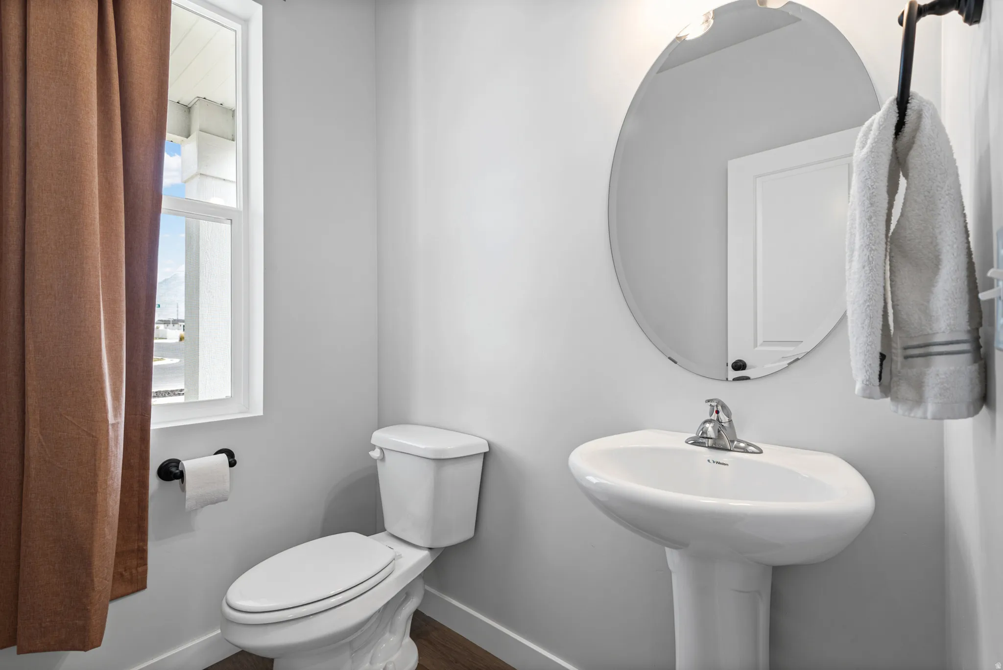 Clean and functional half bath featuring a pedestal sink with chrome faucet, white ceramic toilet with seat, and an oval frameless mirror