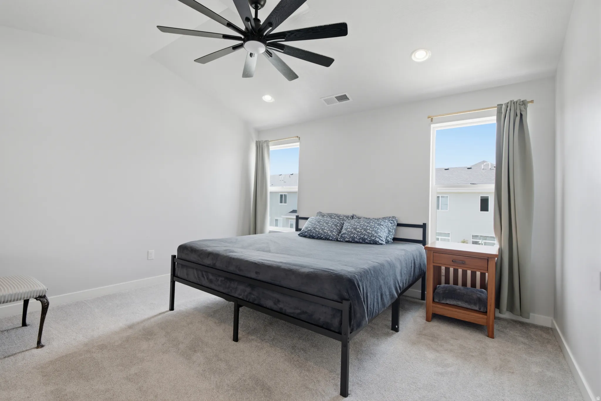 Bright secondary bedroom featuring large dual windows with natural light, neutral carpet flooring, and modern ceiling fan with integrated lighting
