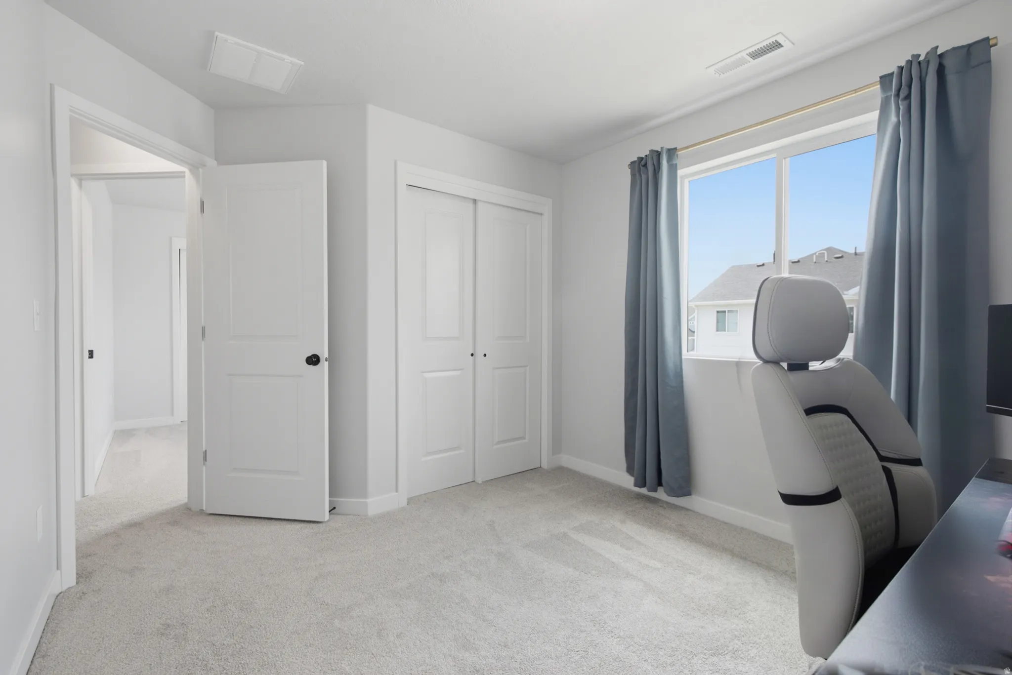 Bright secondary bedroom with neutral carpet flooring, multiple white six-panel closet doors providing ample storage, large window with blue-toned curtains, and recessed ceiling lighting