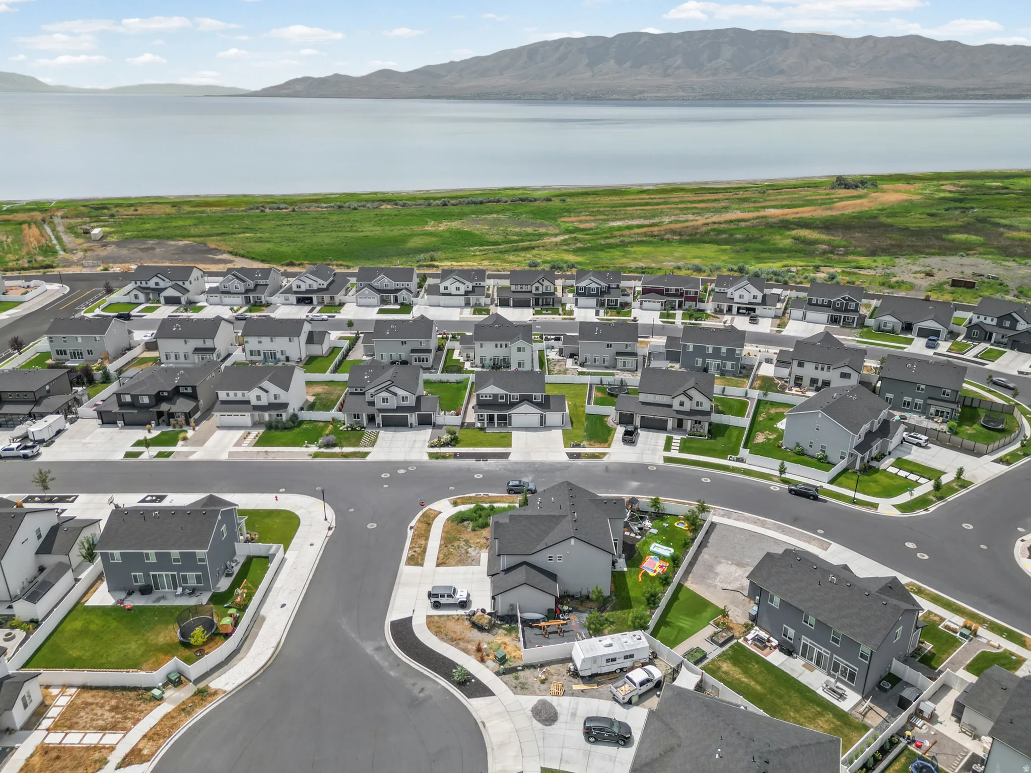 Aerial view of a newly developed residential community featuring modern homes with charcoal and light gray exterior finishes, manicured lawns with landscape plantings, and paved streets with curved design elements