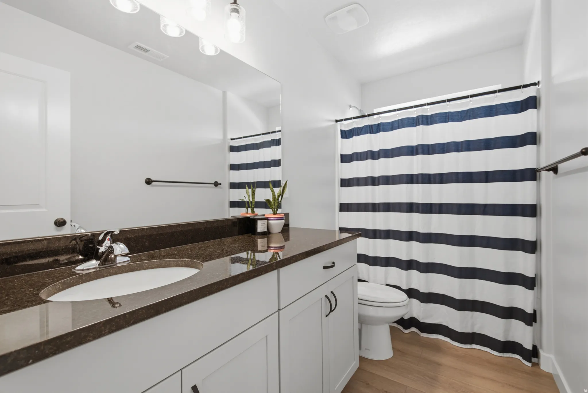 White vanity with dark countertop, undermount sink, and chrome faucet