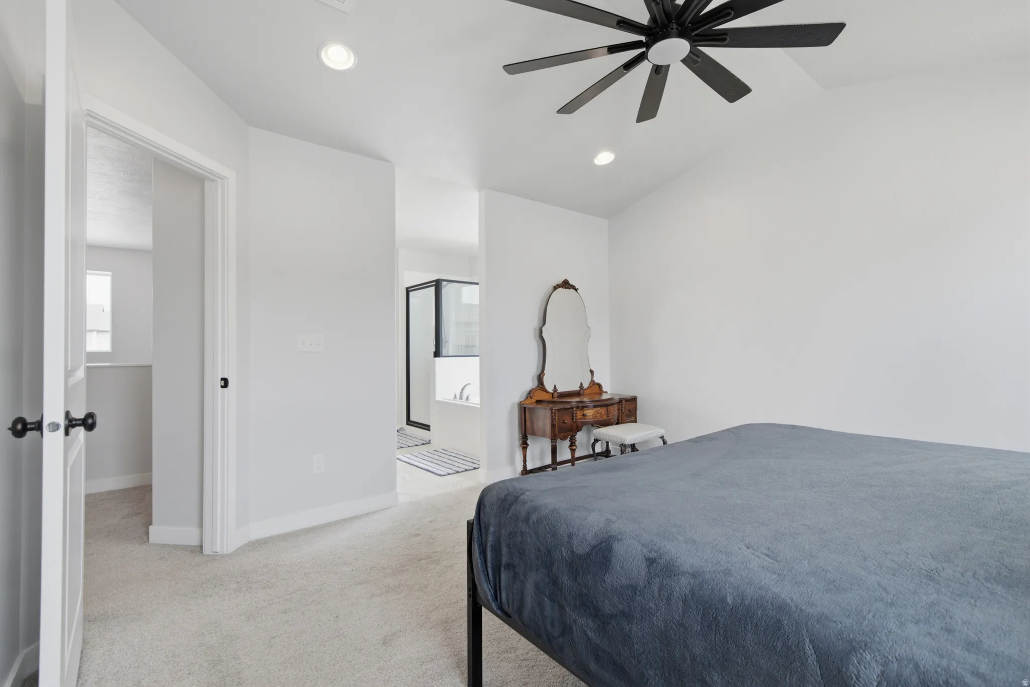 Vaulted ceiling, recessed lighting, ceiling fan, plush carpet, and a walk-in shower with black-framed glass
