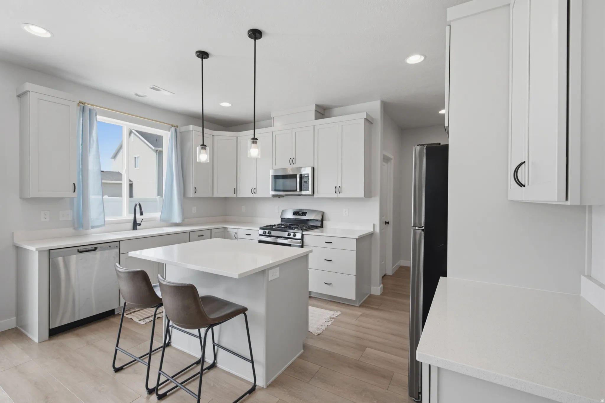 Modern kitchen featuring white cabinetry, quartz countertops, and stainless steel appliances including a gas cooktop and microwave