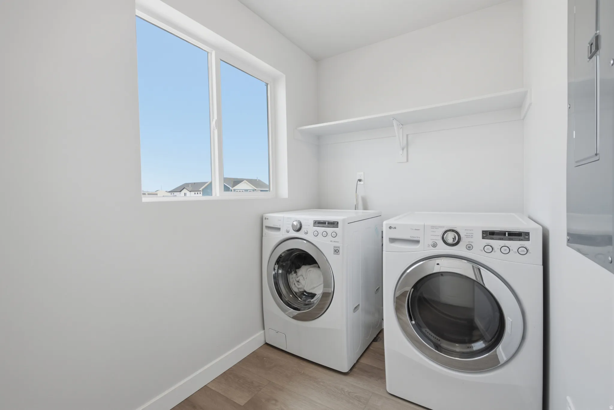 Laundry area featuring wood-finish flooring, a white window frame, and an integrated shelf