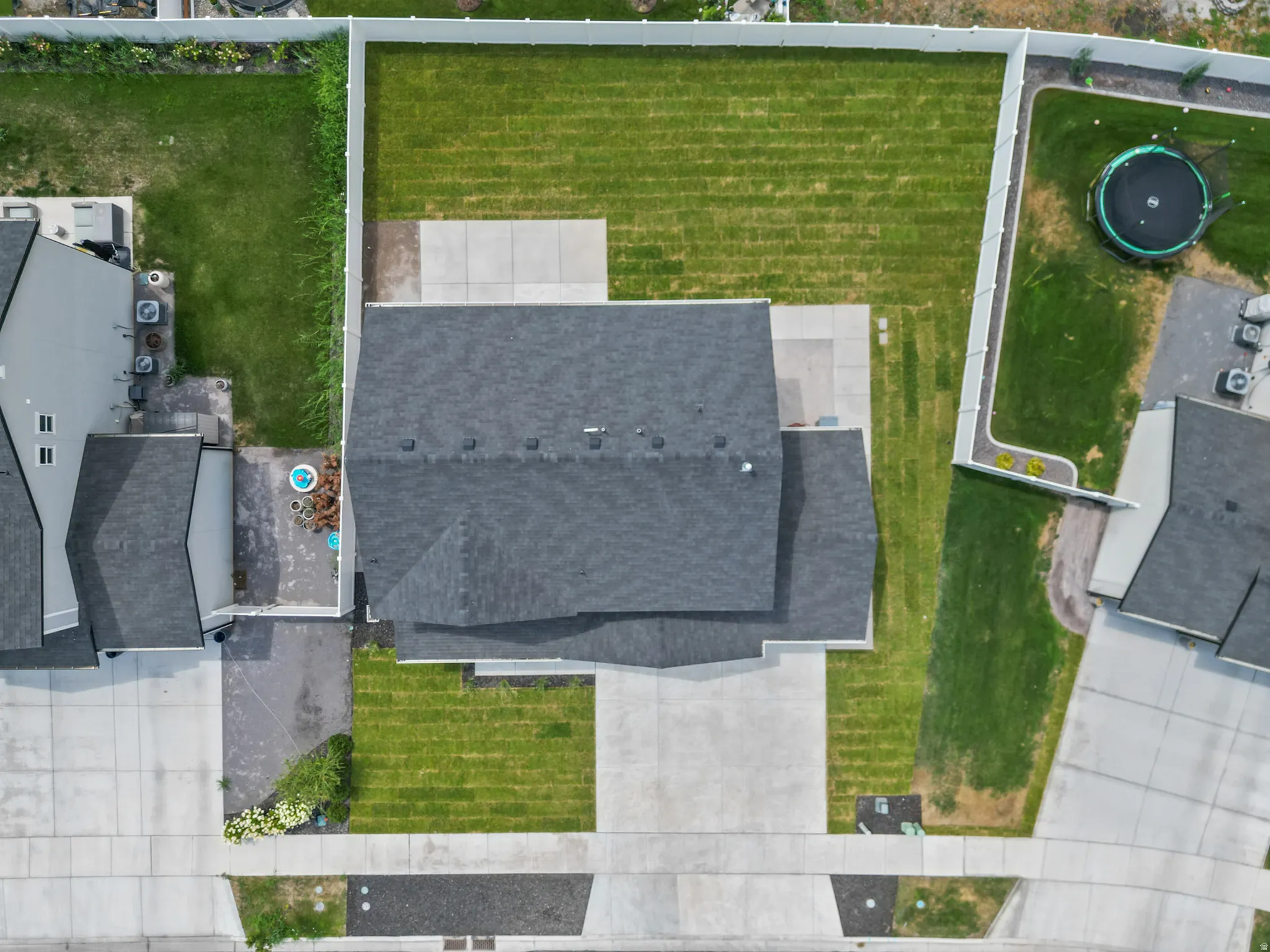 Dark gray shingle roof, white privacy fencing, concrete patio, concrete driveway, and a grass lawn