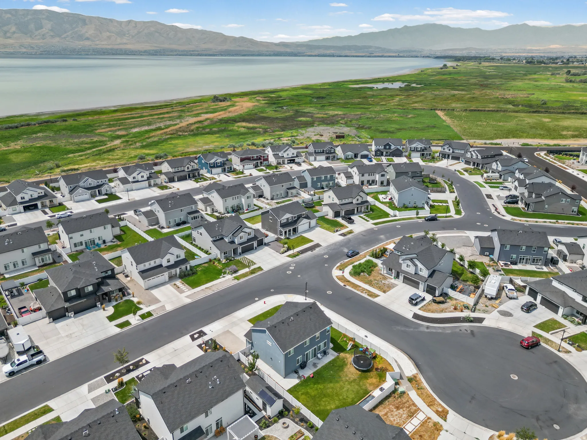 Residential community with paved roads, green landscaping, and surrounding mountainous terrain and a large body of water
