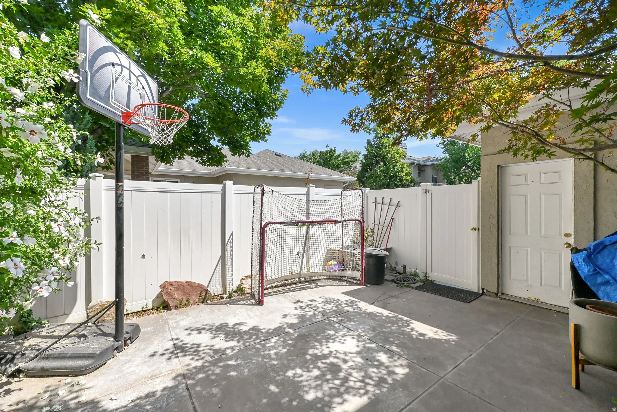 Expansive concrete patio with mature tree coverage and white vinyl fencing