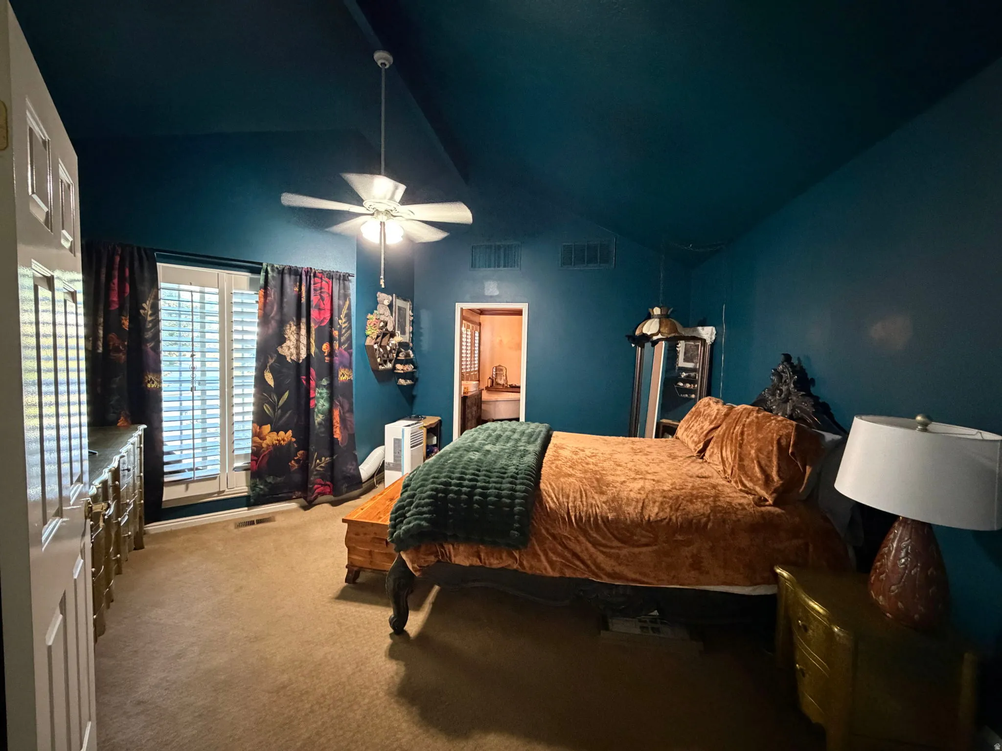 Vaulted ceiling with a ceiling fan, window with white plantation shutters, and wall-to-wall carpeting