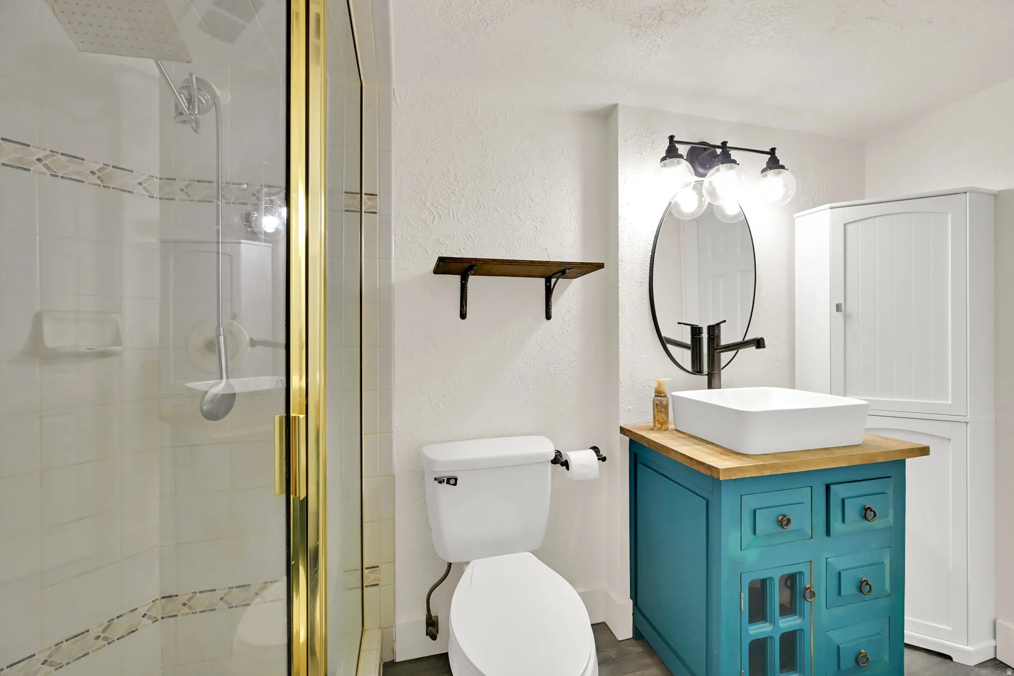 Spa-inspired bathroom featuring a custom teal vanity with wood countertop, vessel sink with matte black faucet and mirror, and a walk-in shower with glass enclosure and brass-framed doors