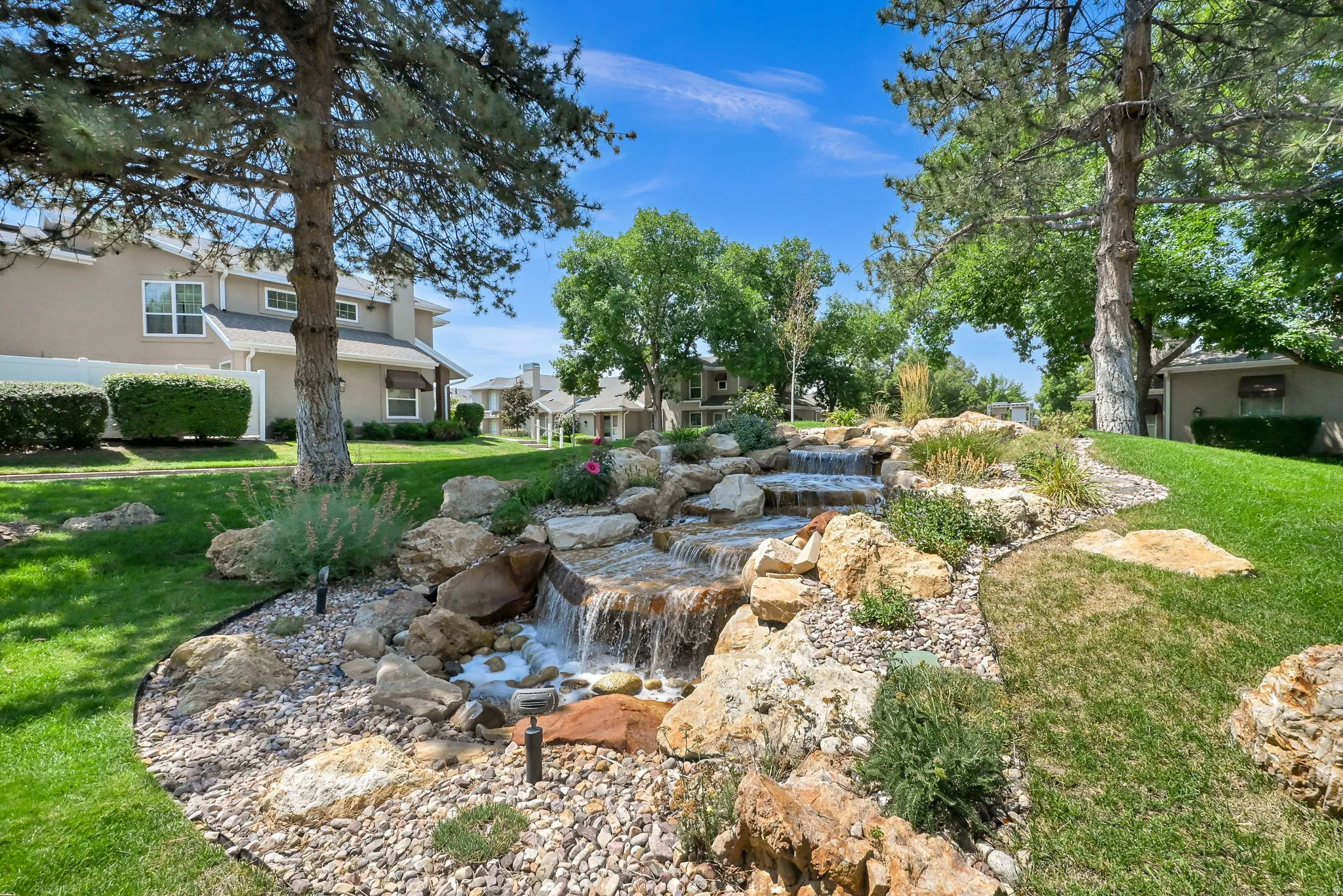 Expansive outdoor space featuring a multi-tiered rock waterfall, mature trees, and a manicured lawn
