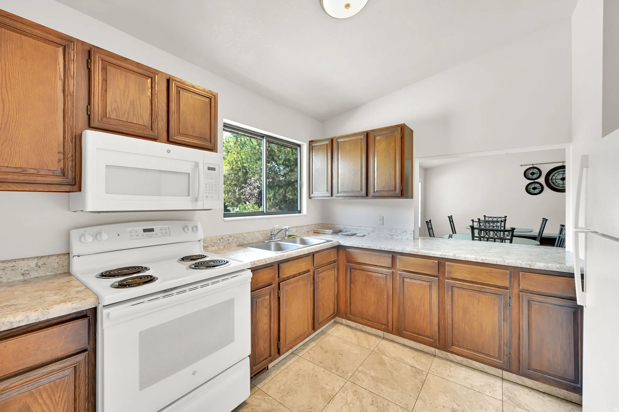 Kitchen featuring wood cabinetry, white appliances, a double basin sink, and tile flooring