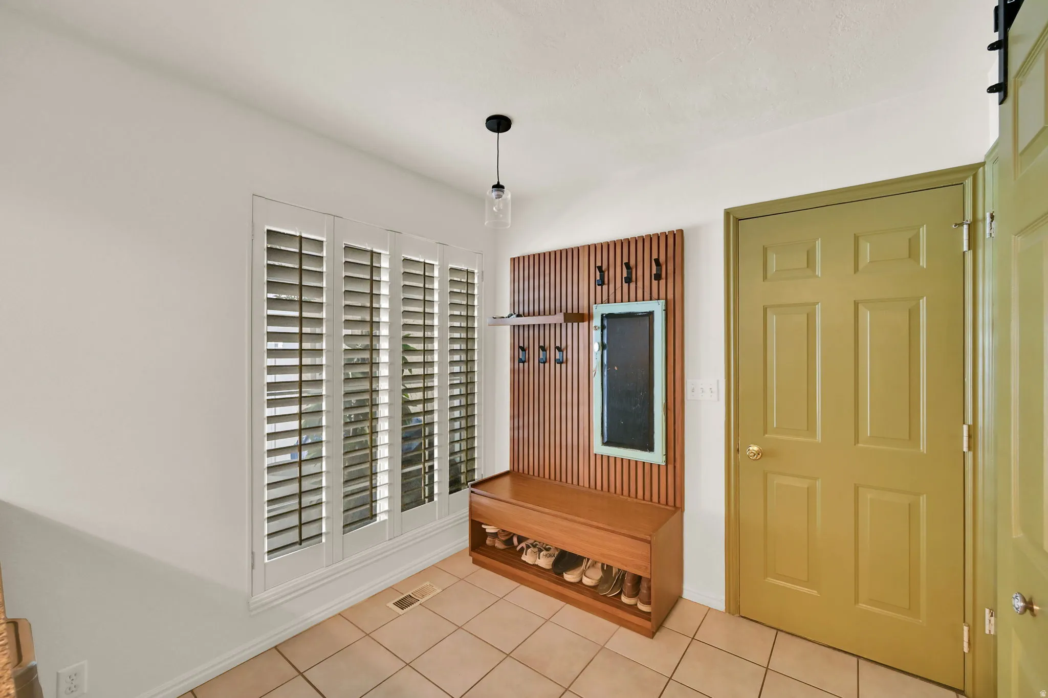 Tiled flooring, bright white walls, decorative wall paneling with integrated hooks, built-in storage bench, and white plantation shutters