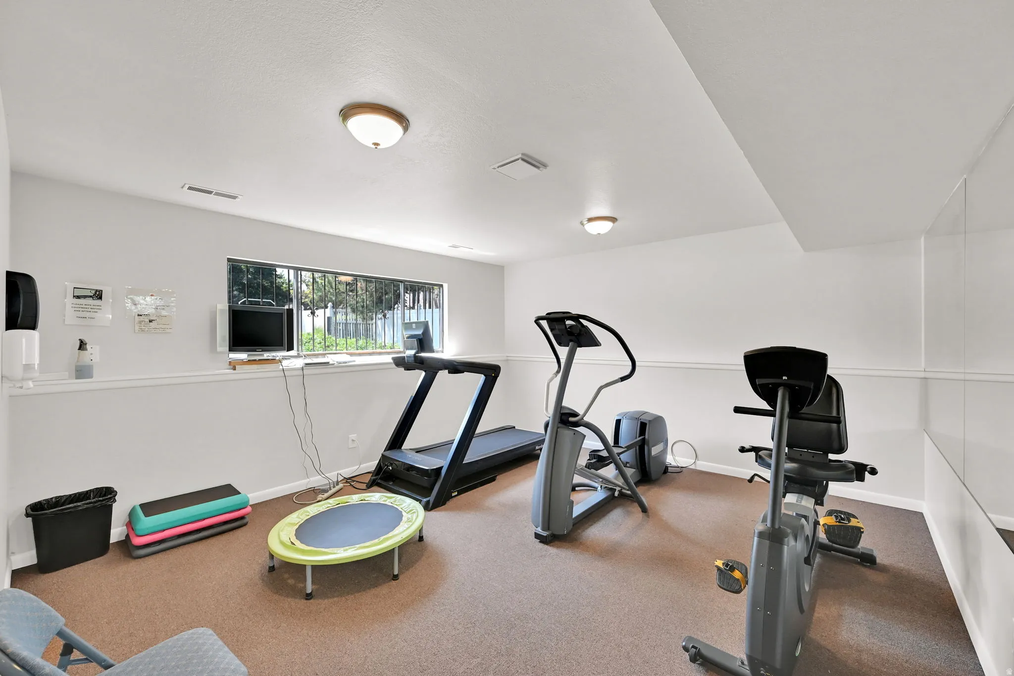 Dedicated home fitness room featuring cork-finish flooring, recessed and flush-mount ceiling lighting, large operable window with natural light, white shiplap wall paneling, and ample space for multiple exercise stations and equipment