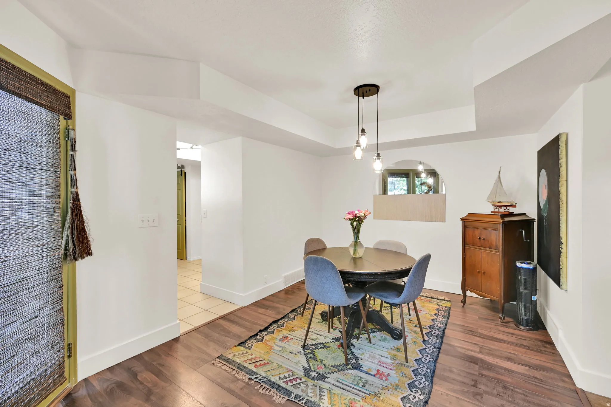 Wood-finish flooring with white baseboards, recessed ceiling details, archway window, and a modern pendant light fixture