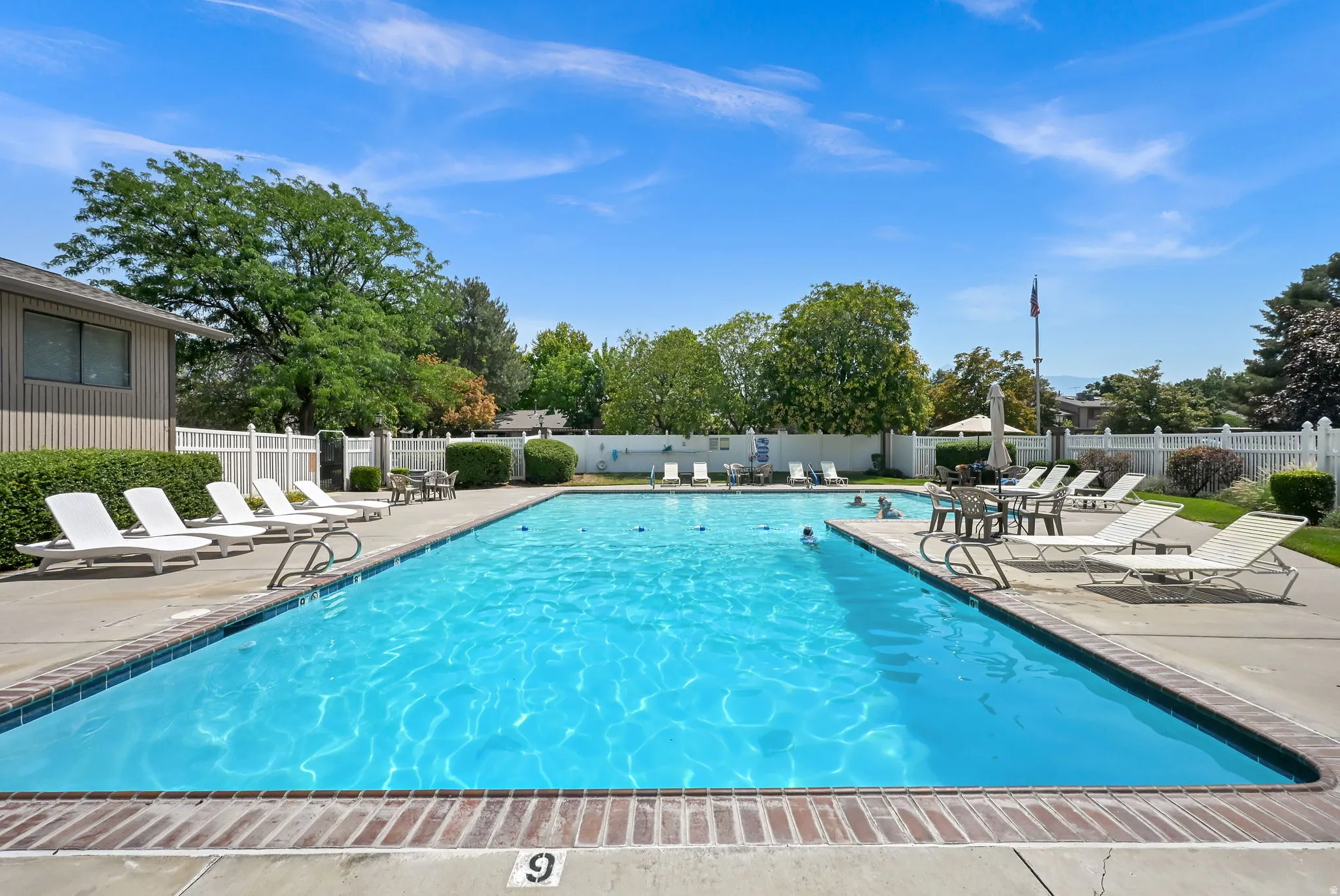 Outdoor swimming pool with a brick coping, concrete surround, and white picket fencing