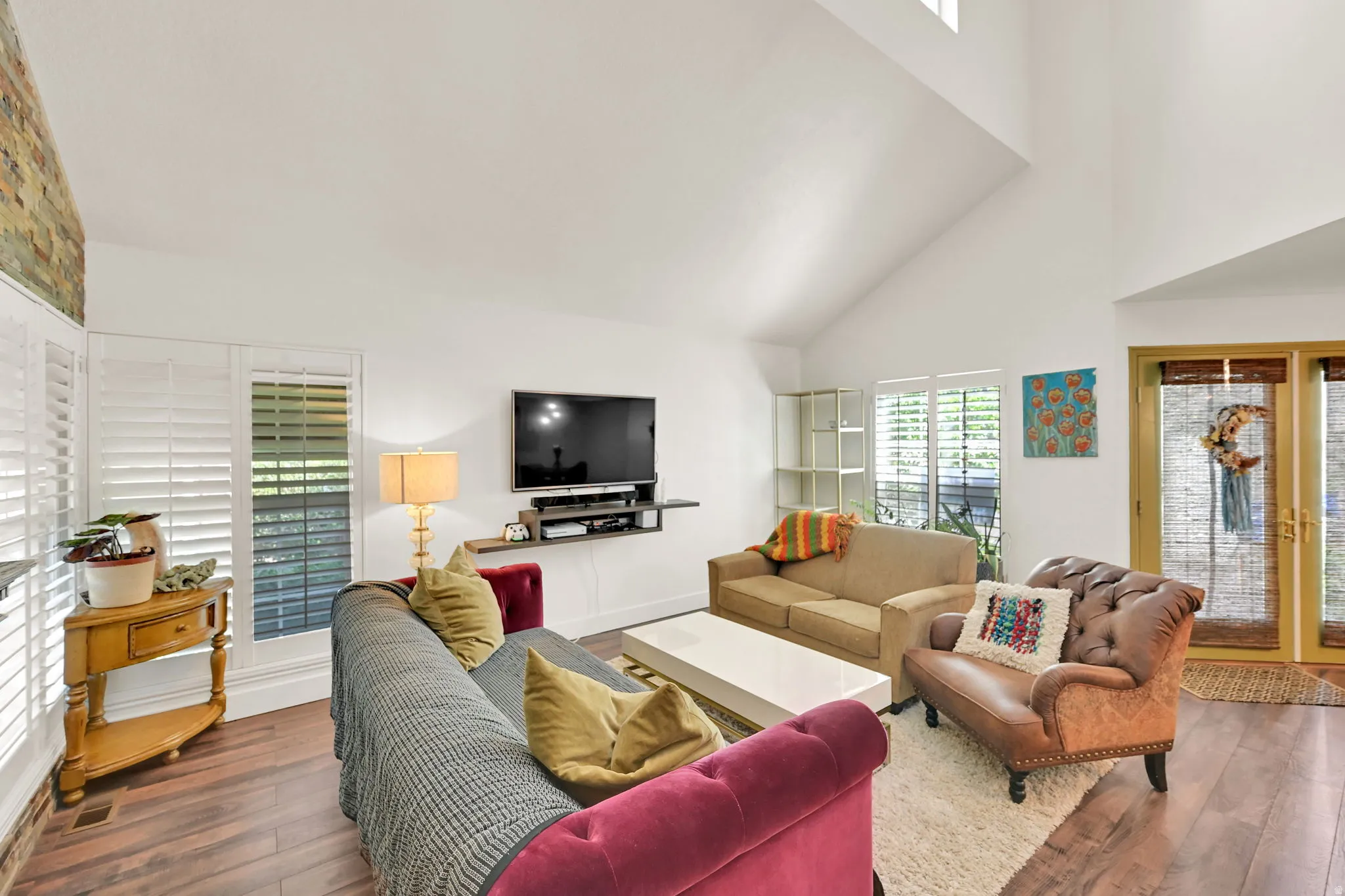 Vaulted ceiling, wood-finish flooring, white plantation shutters, double French doors, and a stone-clad accent wall
