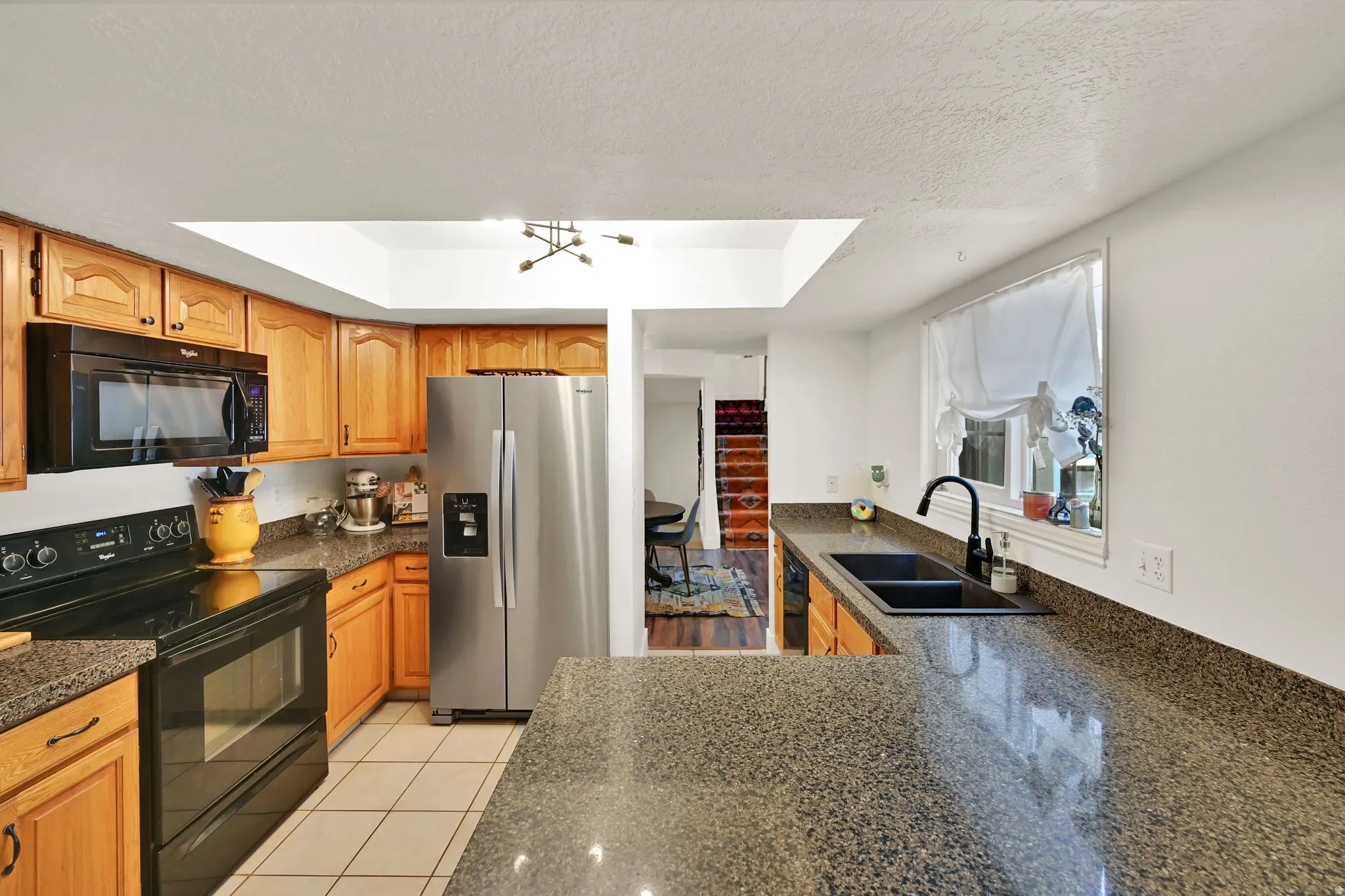 Kitchen featuring wood cabinetry, dark speckled countertops, tile flooring, and a stainless steel refrigerator