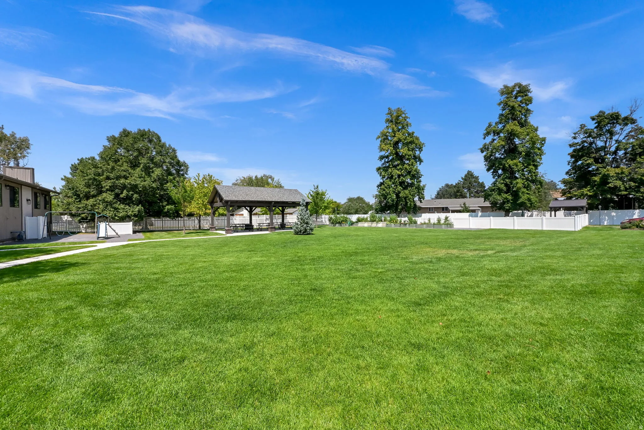 Expansive manicured lawn anchored by mature trees and bordered by white fencing, with detached outbuildings and structures visible across the grounds