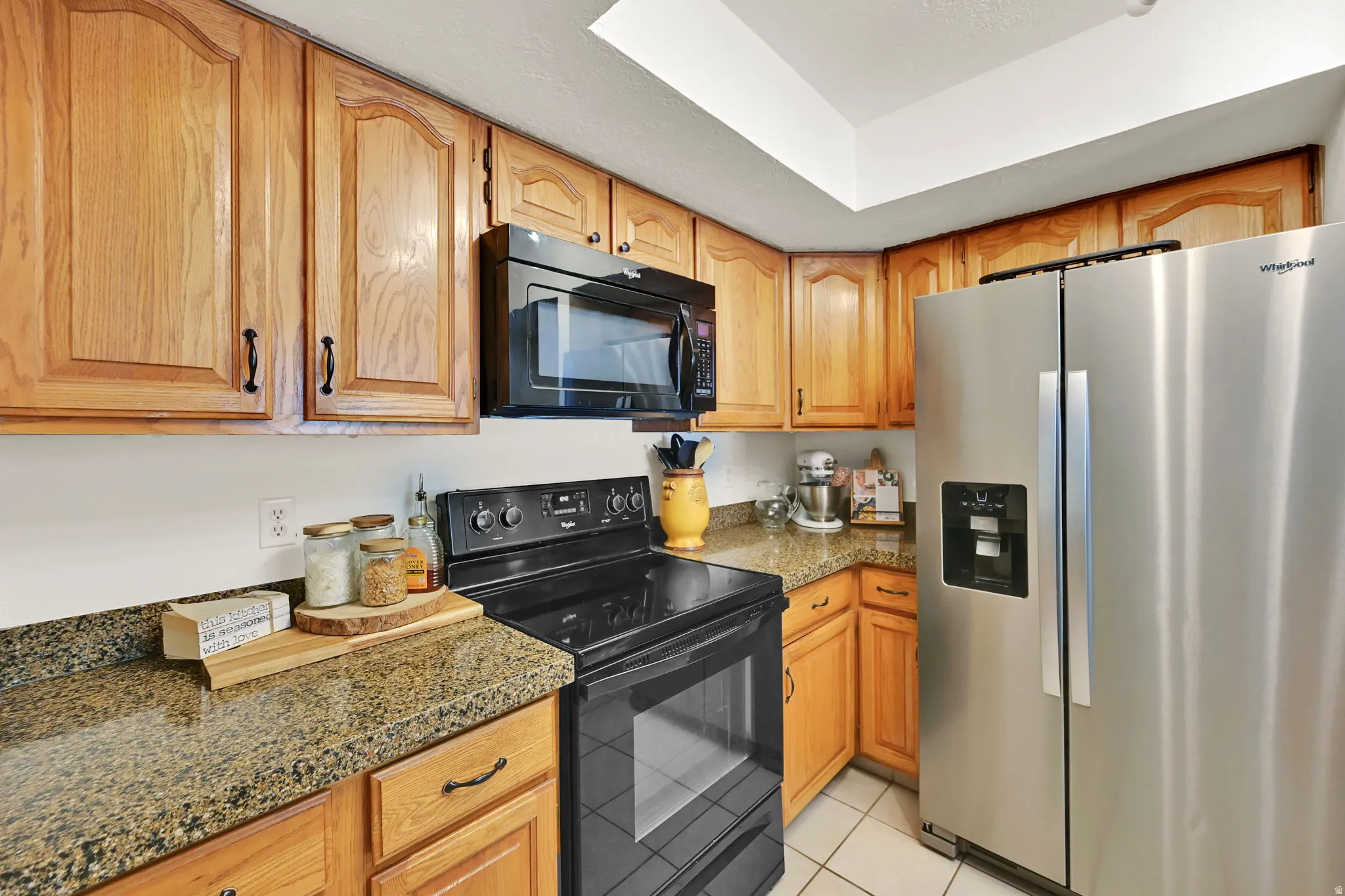 Warm wood cabinetry and granite countertops define this well-appointed kitchen, featuring stainless steel appliances, including a side-by-side refrigerator and black electric range with convection oven