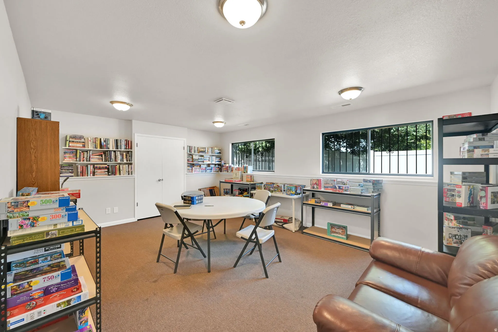 Versatile recreational room featuring cork flooring, recessed ceiling lighting, large windows with security bars, built-in shelving and storage cabinetry, and ample space for multiple uses