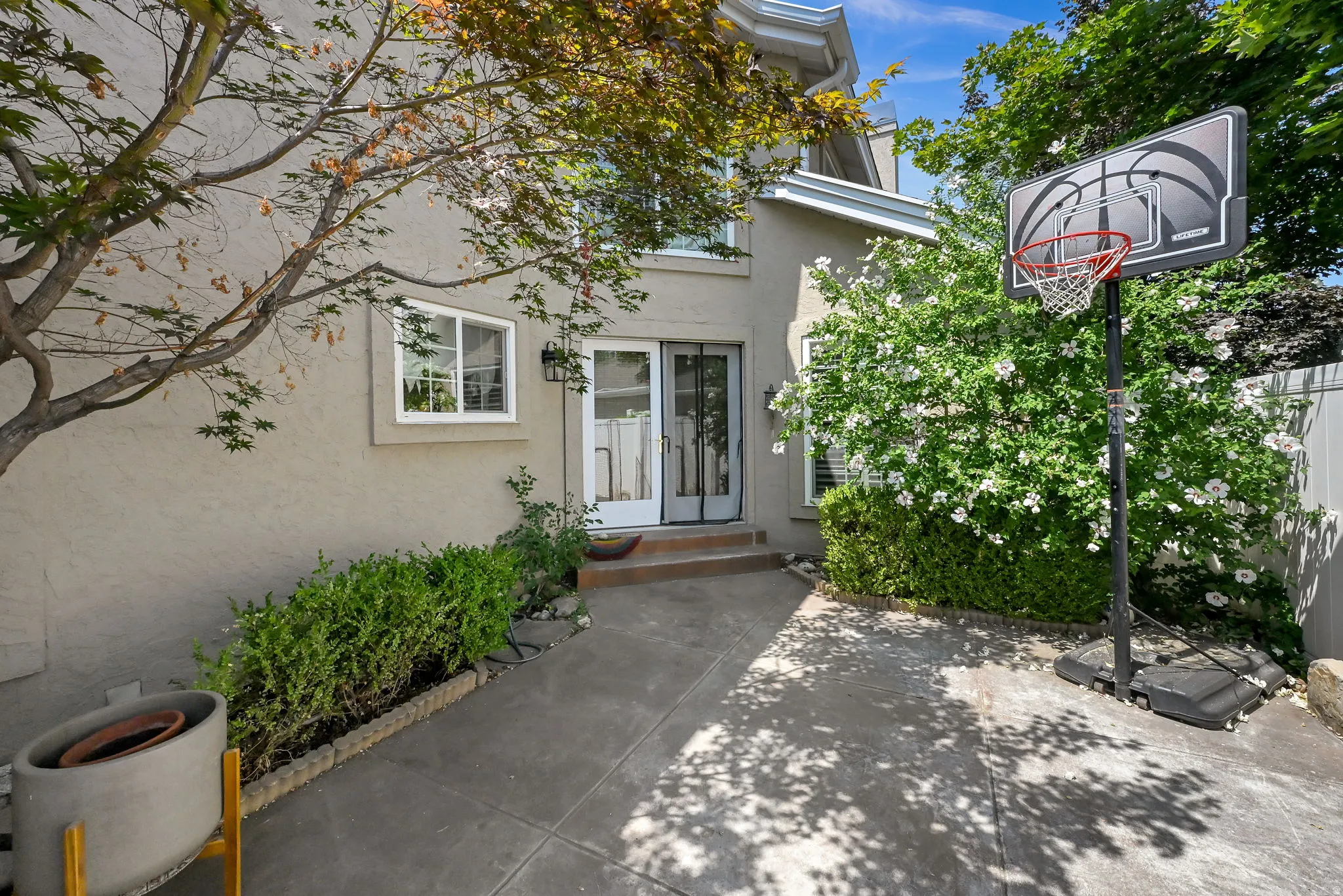Welcoming courtyard entry featuring a dark-finish paved surface, mature landscaping with ivy-covered walls, and a basketball hoop