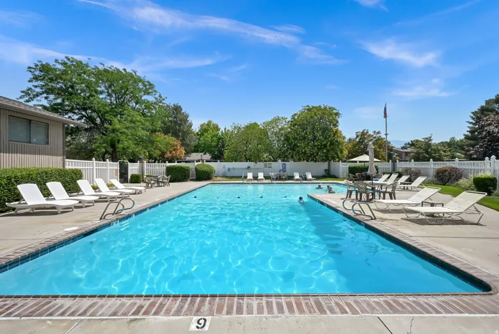 Outdoor swimming pool with a brick coping, concrete surround, and white picket fencing