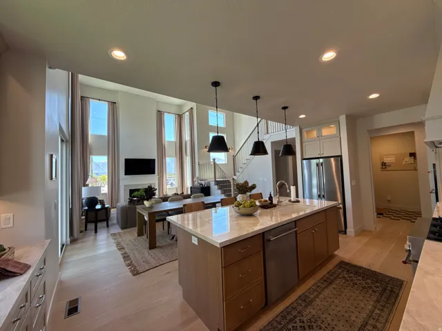 Open-concept living space featuring a gourmet kitchen island with a built-in sink and stainless steel appliances, wood-finish flooring, a double-height living room with tall windows, a fireplace, and a wood staircase with balusters