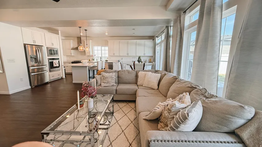 Open-concept living area featuring a sectional seating arrangement, wood-finish flooring throughout, and abundant natural light from expansive windows with contemporary drapery