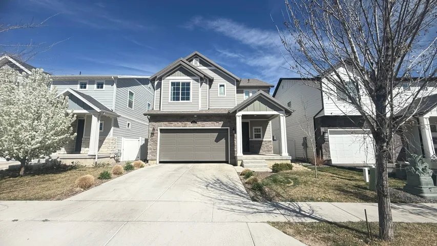 Two-story residence featuring light gray siding with stone accents, a covered front entry, and an attached two-car garage