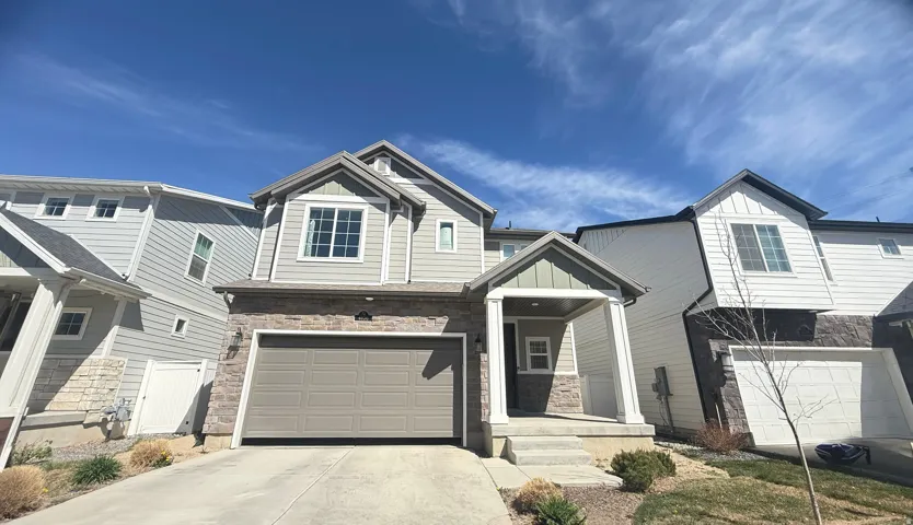 Two-story residence featuring light gray siding with stone veneer accents, a covered front entry, an attached garage, and multiple windows