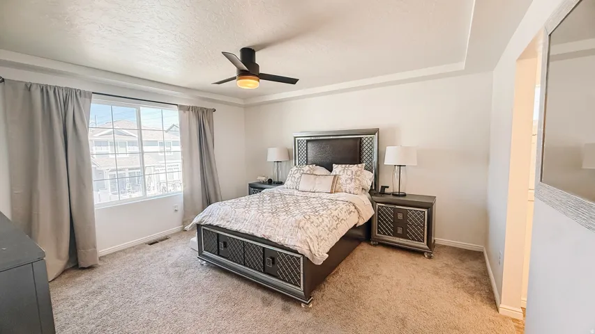 Tray ceiling with a ceiling fan, broad window, and plush carpet flooring