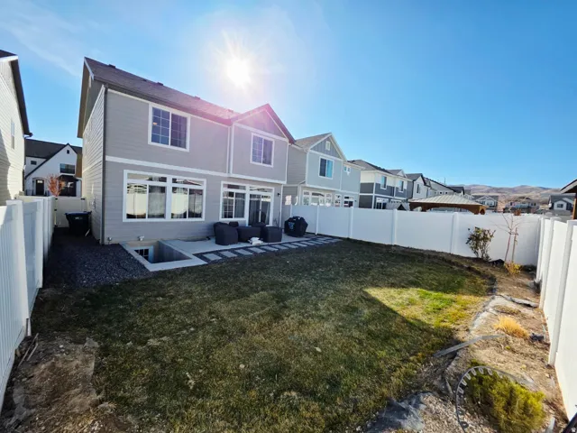 Expansive backyard featuring a manicured lawn, concrete patio, and white privacy fencing
