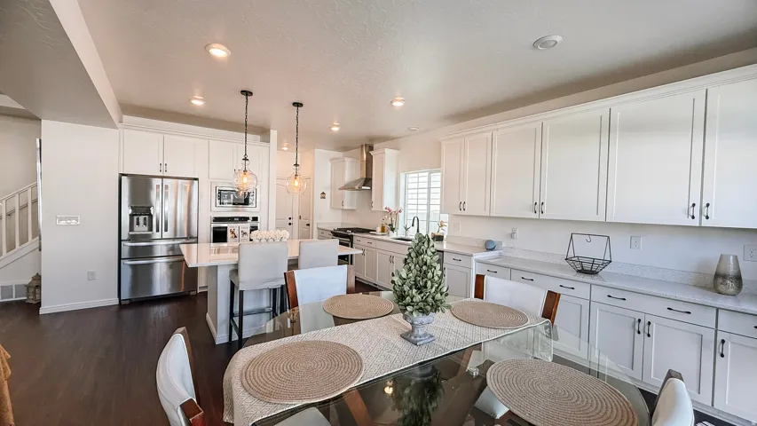 White shaker cabinetry, stainless steel appliances, central kitchen island with seating, pendant lighting, and wood-finish flooring